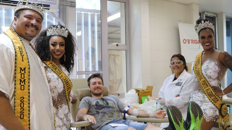 Rei Momo  e duas princesas do carnaval junto com uma técnica de enfermagem e um doador doando sangue no Hemocentro