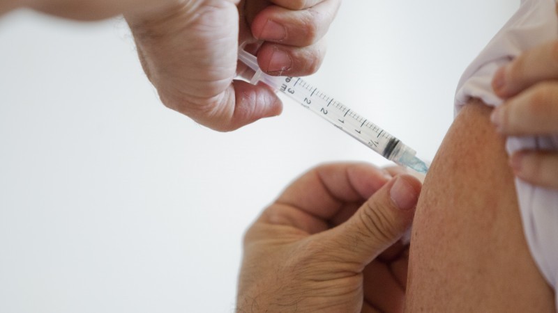 um braço de um a pessoa idosa recebendo a aplicação da vacina por meio de uma seringa