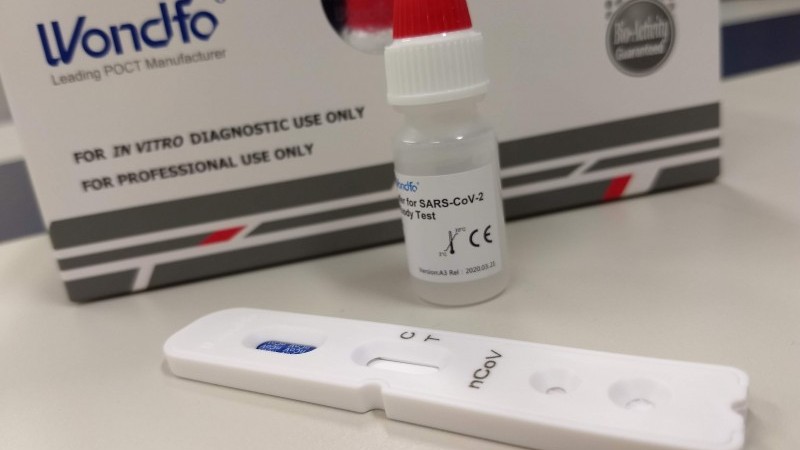 A imagem mostra um frasco e um aplicador de teste rápido de anticorpos, além de uma embalagem.