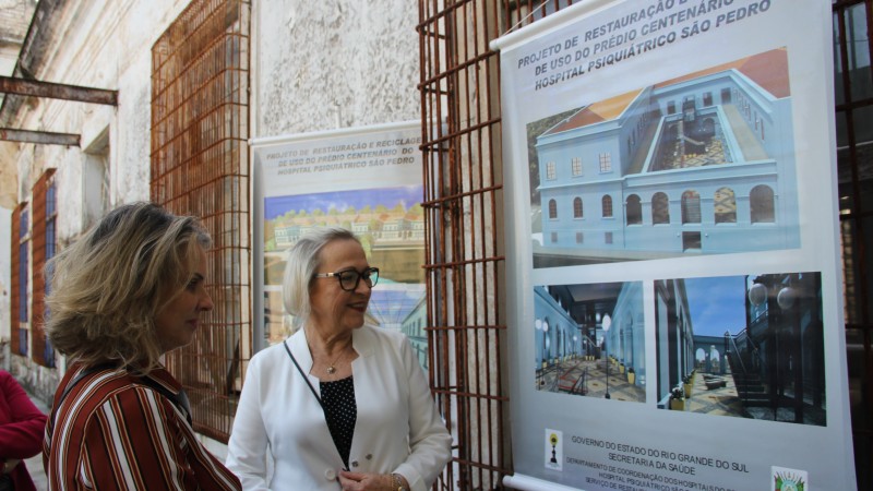 Secretárias Leany e Arita observam banner exposto com informações do projeto de restauração do São Pedro.